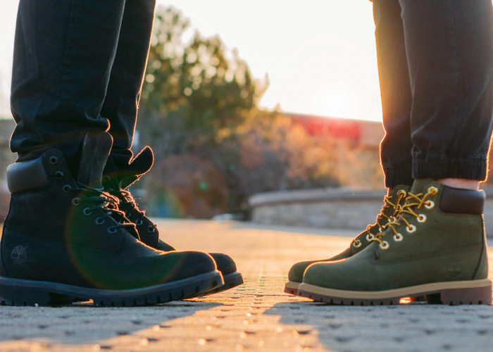 two people wearing green-and-black work boots standing on gray concrete pavement