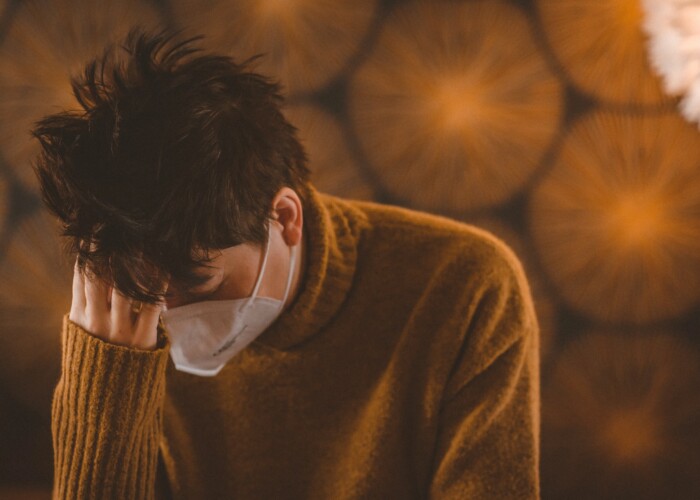 man in brown coat wearing white face mask